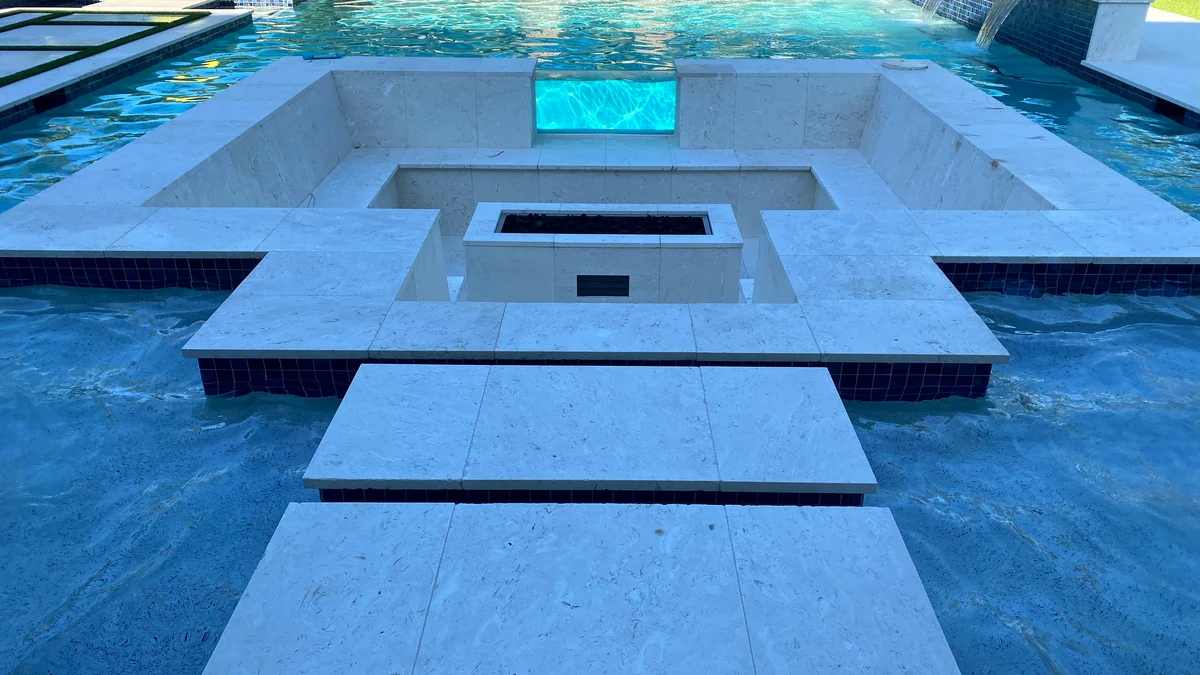Resort pool compound terrace on a Naples estate — fire pit island, spa spill, and continuous hardscape deck