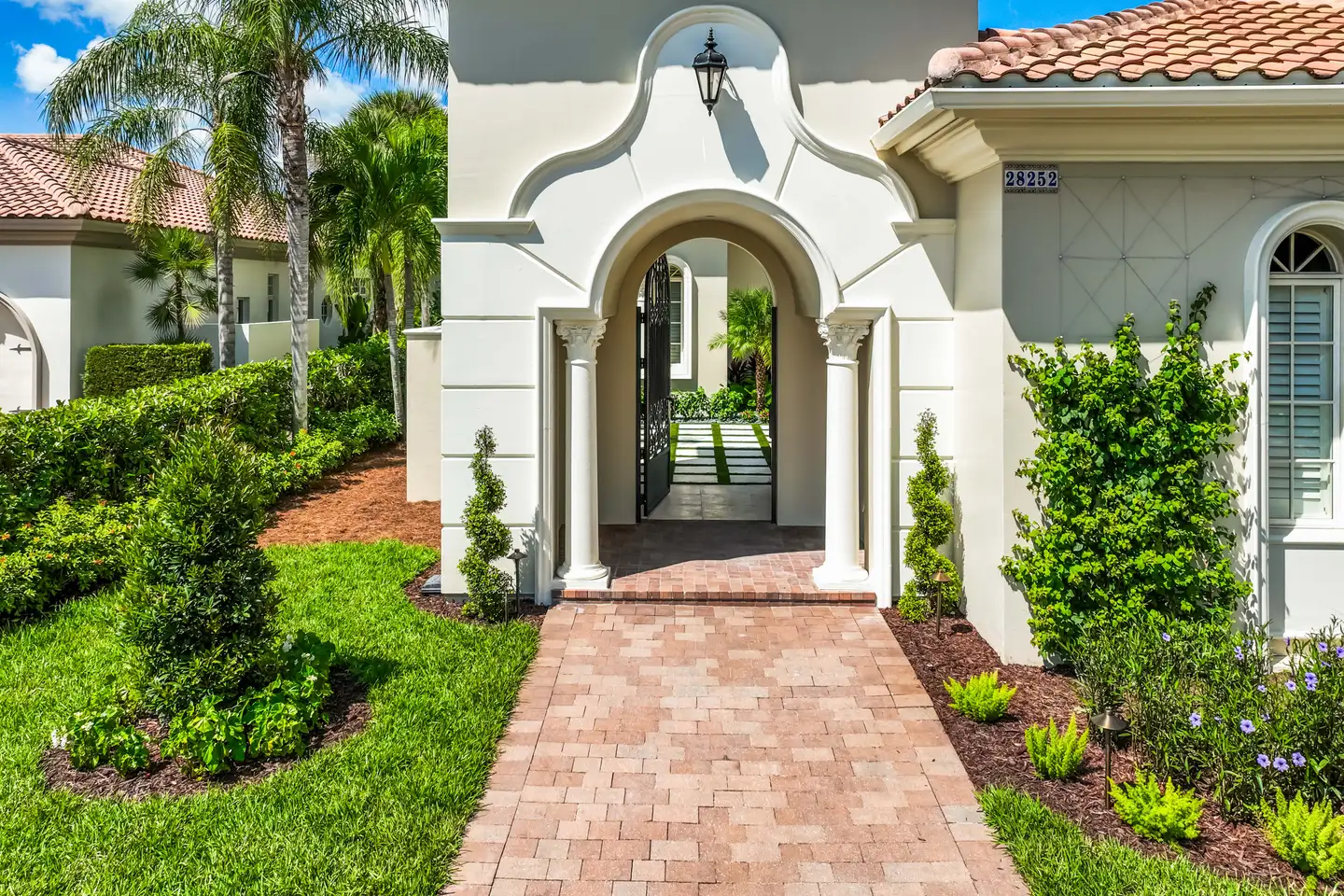 Mediterra estate entry arch — brick paver path, ornate gate, and porte cochère